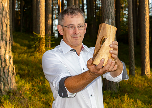 Johann Binder hält eine Vase aus Holz in der Hand.